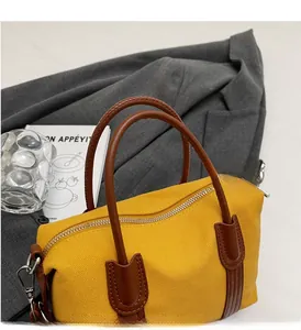 Détail d'un sac en toile jaune avec anses en cuir marron sur un blazer gris chic