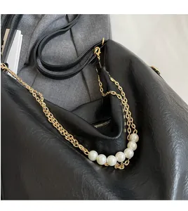 Detail of black leather tote bag featuring golden hardware chains and pearl decorations
