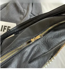 Detail of smooth gold zipper and pearl chain on black textured retro tote bag