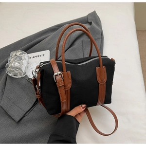 Détail du sac à main en toile noire avec poignées en cuir marron et zip argenté