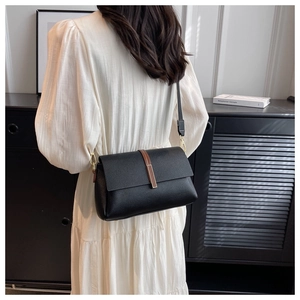 Detail of black lychee grain leather crossbody bag with brown accent and metal buckle