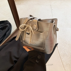 Silver crocodile pattern bucket bag with pearl bow charm held by a model in a mirror