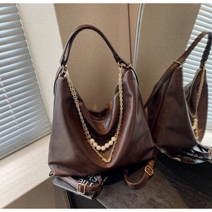 Detail of dark brown leather bag with vintage texture and gold pearl chain decoration