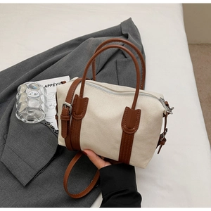 Gros plan d'un sac Boston en toile crème avec finitions en cuir marron et boucles argent