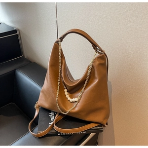 Detailed shot of brown textured tote bag featuring gold chain and white pearl accents