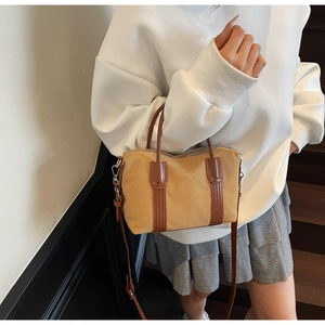 Détail du sac Boston en toile porté en bandoulière sur un mannequin aux tons kaki et marron