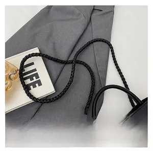 Close-up of black leather bag featuring woven strap and golden knot metal buckle detail