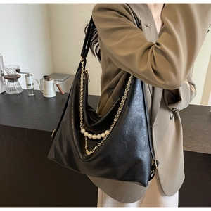 Detail view of a large black leather hobo bag with gold chain and pearl charms on shoulder