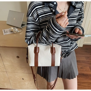 Détail d'un sac Boston en toile et cuir porté par un mannequin avec bandoulière réglable