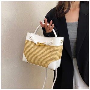 Detail of straw woven tote with white leather trim and golden metal knot buckle