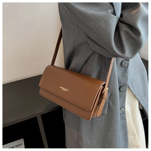 Close-up of brown leather shoulder bag featuring gold fashion typography and neat stitching