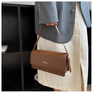 Detail of coffee brown baguette bag with golden fashion text and elegant metal buckle