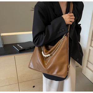 Detail of brown leather tote bag featuring elegant pearl and gold chain decorations