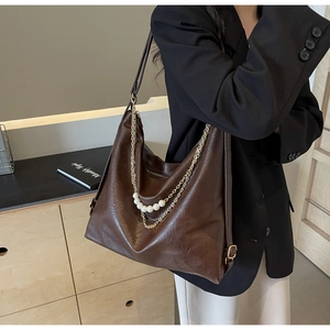 Close-up of vintage brown leather tote bag featuring gold chain and pearl decorative charms