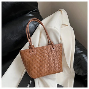 Détail du sac cabas tressé marron avec nœud de poignée sur tissu de blazer blanc