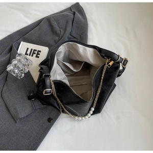 Detail of black textured leather tote featuring elegant gold chain strap with white pearls