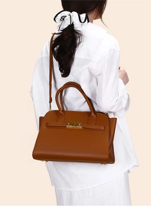 Detailed view of brown litchi leather tote bag with gold metal clasp on white shirt