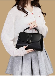Detail of a chic black leather handbag with a gold ring clasp held by a model