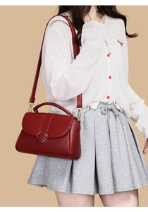 Detail of red leather bag with golden round buckle worn by model on solid background