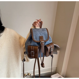 Close-up of blue denim backpack featuring brown leather pockets and contrast stitching