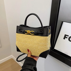 Woven straw handbag with black leather trim and gold twist buckle in modern interior