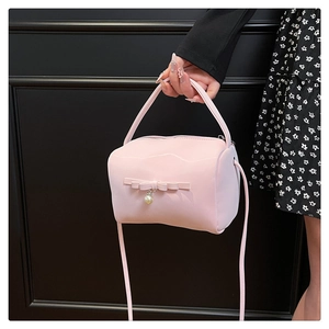 Nahaufnahme der rosa Lackleder-Handtasche mit Schleife und Perle, gehalten von einem Model