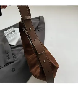 Détail du sac à bandoulière en daim marron foncé avec rivets métalliques sur la lanière