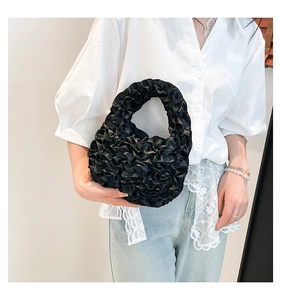 Close-up of black pleated ruffle handbag with satin finish held by a model in white