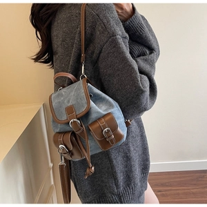 Detail view of denim mini backpack with brown leather trim worn by a model in soft light