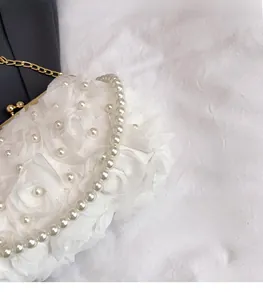 Close-up of white floral handbag featuring chiffon flowers, pearls and gold hardware