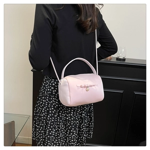 Detail der rosa Satin-Zylindertasche mit Schleife und Perlenanhänger vor dunklem Hintergrund