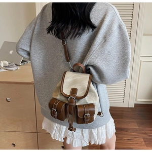 Detail view of mini canvas and brown leather backpack worn by a model in a home setting