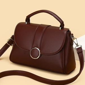 Dark brown matte leather handbag with metal ring and shoulder strap on geometric stand
