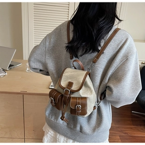 Rear view of a vintage beige canvas backpack with brown leather trim worn by a model