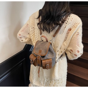 Detail of gray canvas backpack with brown leather trim worn by a model in casual knitwear