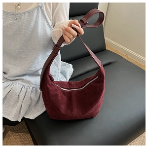 Détail du sac hobo en daim bordeaux avec bandoulière réglable sur un canapé noir