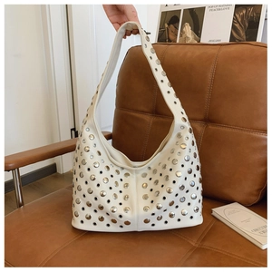 Détail d'un sac hobo blanc de style punk avec des clous en métal argenté sur une chaise
