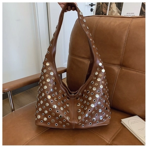 Gros plan sur sac demi-lune en cuir marron avec rivets argentés sur sofa chic