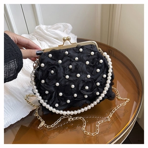 Close-up of black 3D floral evening bag with pearl handle and golden chain on table