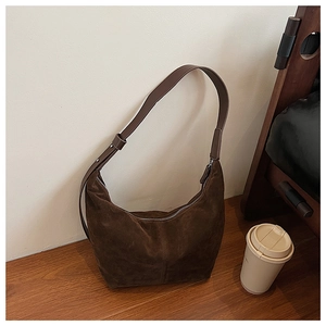 Gros plan d'un sac hobo en daim marron foncé avec bandoulière en cuir sur bois