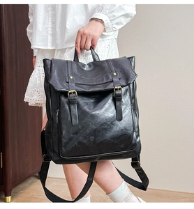 Detail shot of the black leather backpack's pebbled texture and dual buckle closure design