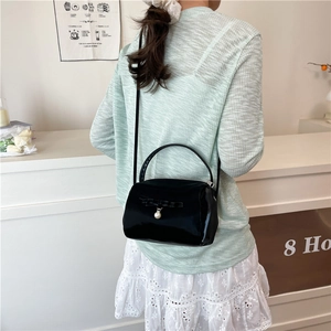 Elegante schwarze Glanzhandtasche mit Schleife und Perle, getragen zu einem hellgrünen Oberteil