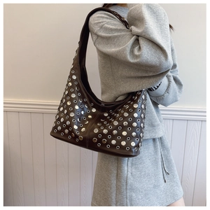 Détail du sac hobo marron foncé avec des rivets argentés porté à l'épaule par un mannequin