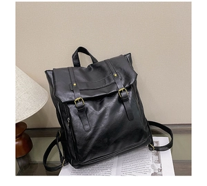 Detail of black vintage faux leather backpack with bronze buckles on a glass surface