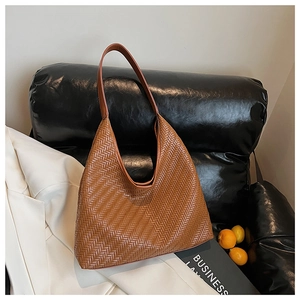 Brown woven hobo bag with V-shaped pattern on a black leather cushion with lifestyle props