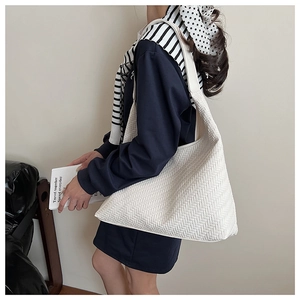 Detail of white oversized woven shoulder bag with herringbone texture worn by model