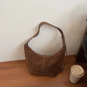 Sac hobo rétro en daim caramel avec bandoulière en cuir sur une table en bois