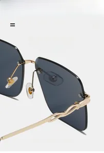 Détail de lunettes de soleil hexagonales sans monture avec branches dorées ondulées et verres gris