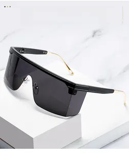 Detail of oversized shield sunglasses with black lenses and gold metal temples on marble