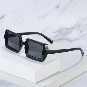 Trendy square black frame sunglasses with dark lenses on a white marble stone display